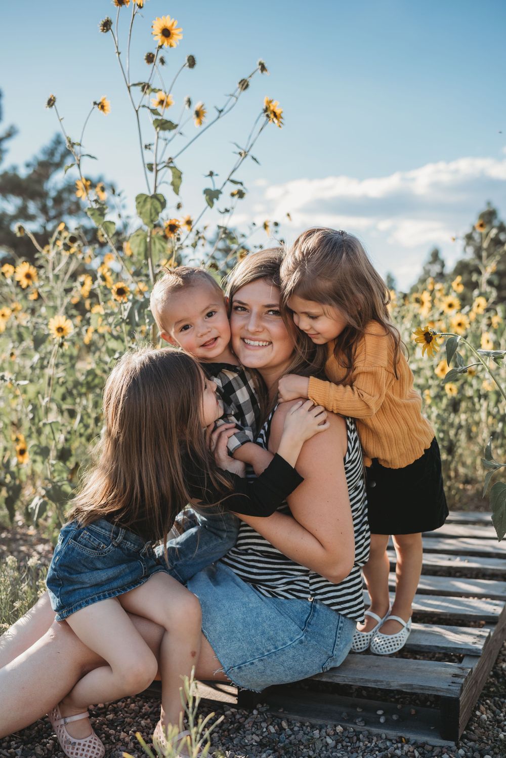 Group embracing on wooden platform in sunflower field during golden hour.