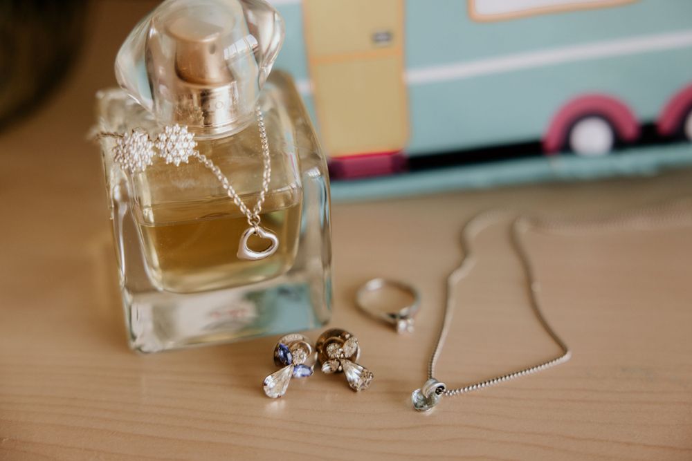 Wedding accessories including perfume bottle, earrings and delicate necklace on wooden surface.
