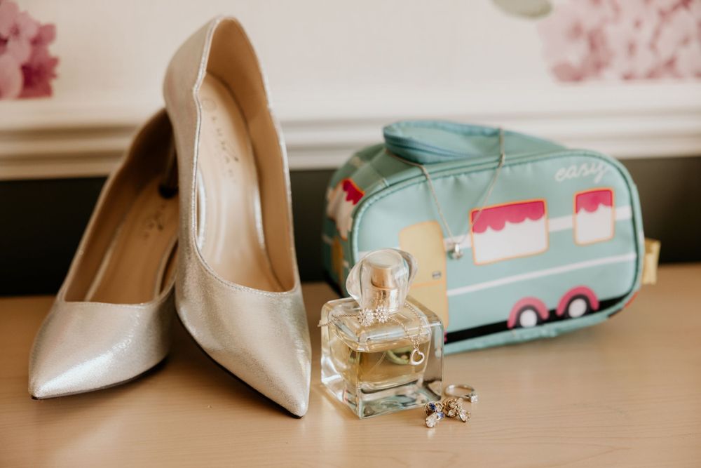 Bridal shoes and perfume bottle beside cute camper van toiletry bag.
