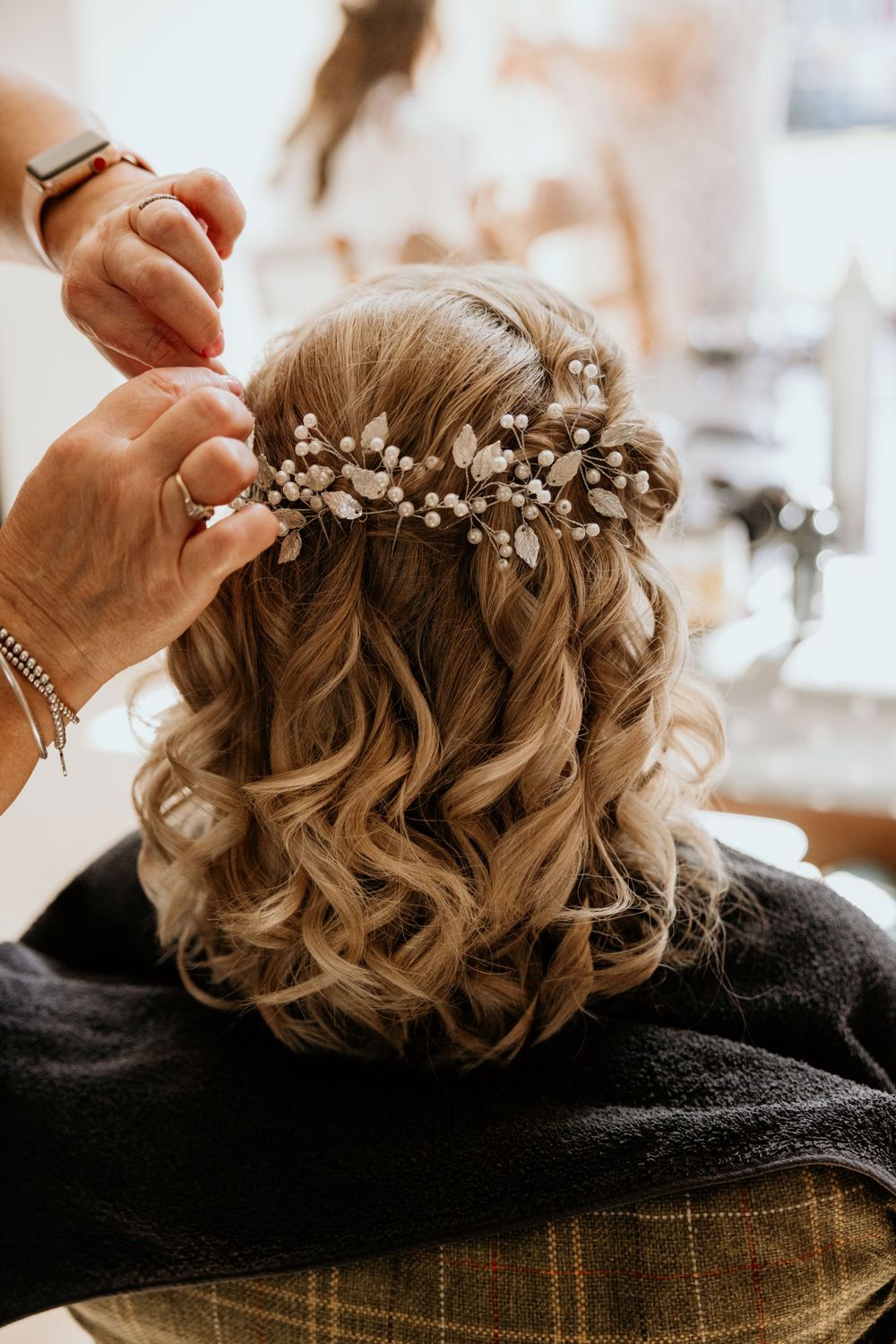 Detailed shot of bridal hairstyling with pearl accessories being placed in curled blonde hair.