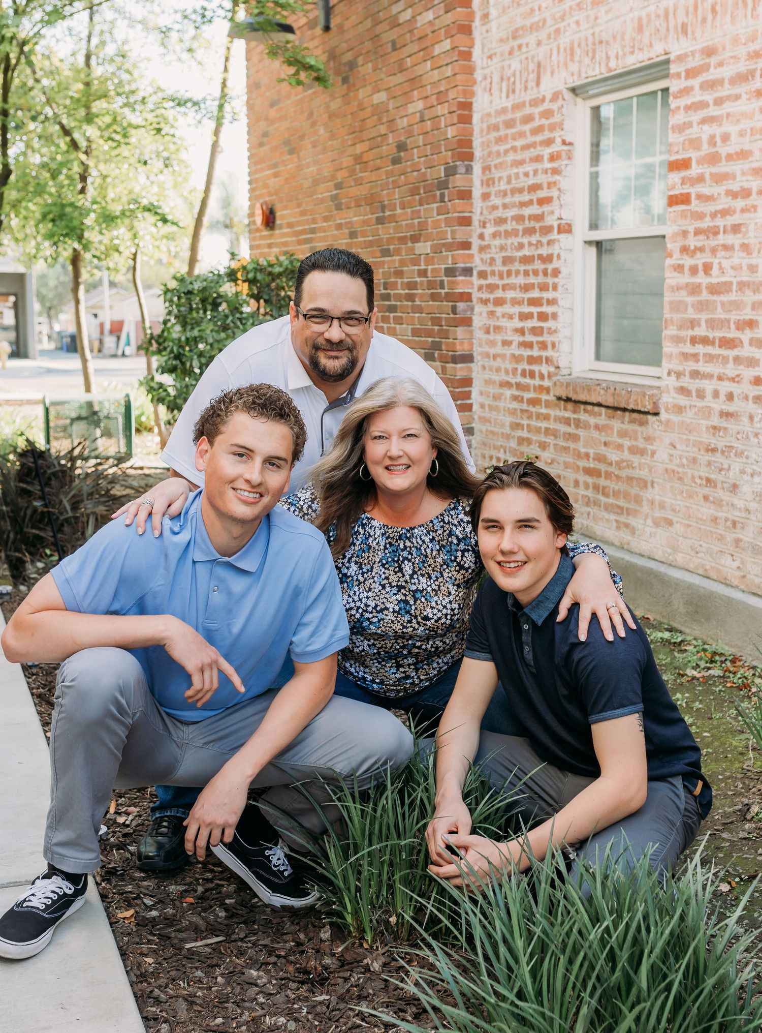 Four people squatting in a planter near a brick building