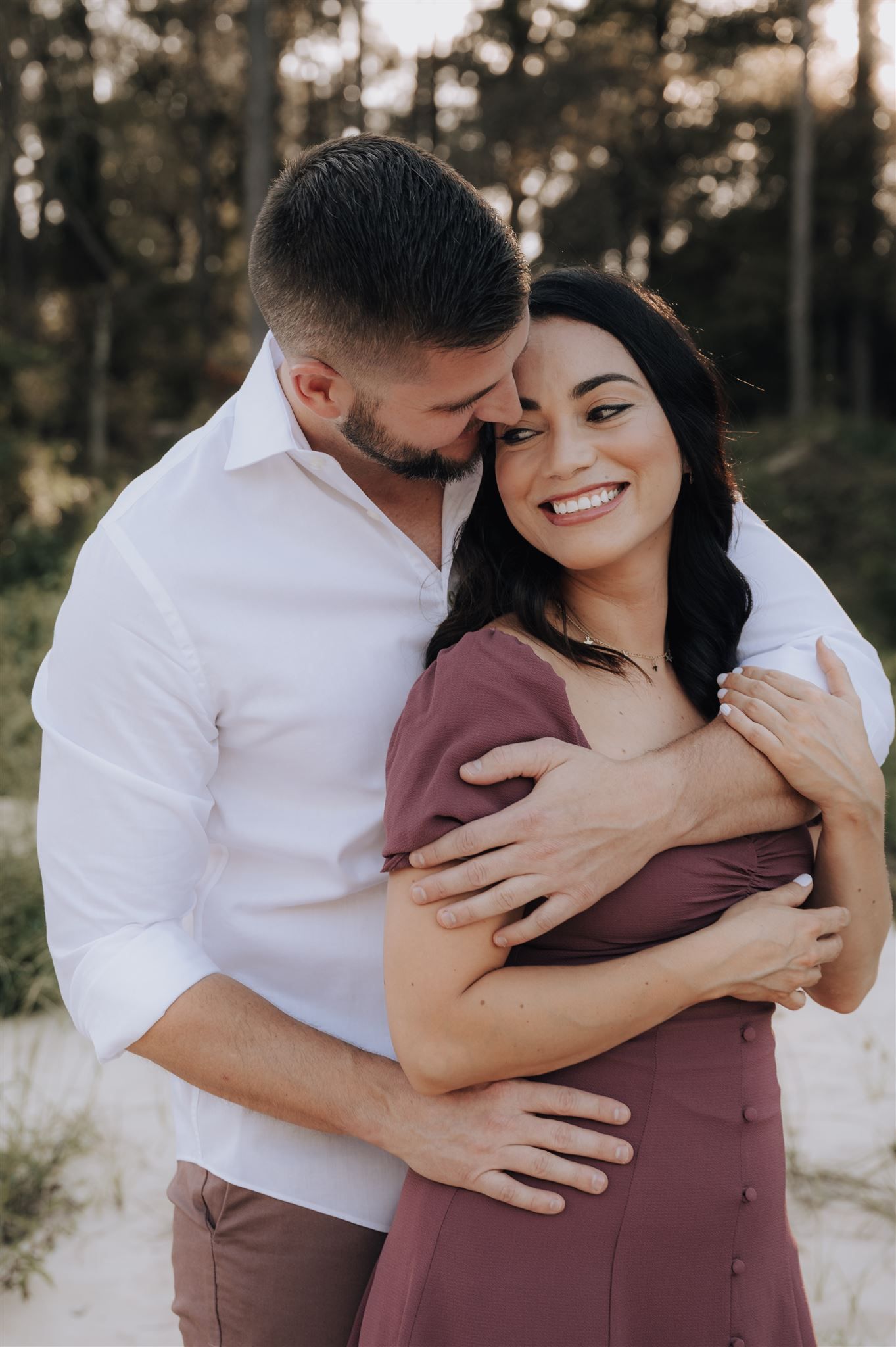 A couple embraces intimately outdoors with natural forest scenery in the background.