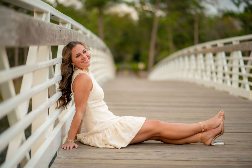 Woman in white sundress relaxes on white wooden bridge.