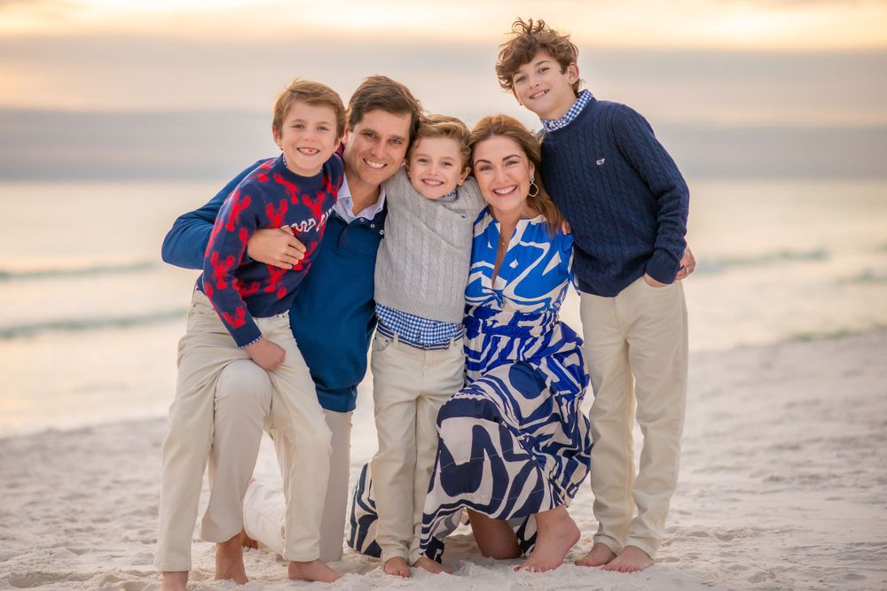 Family group poses together on beach at sunset wearing coordinated blue and white outfits.