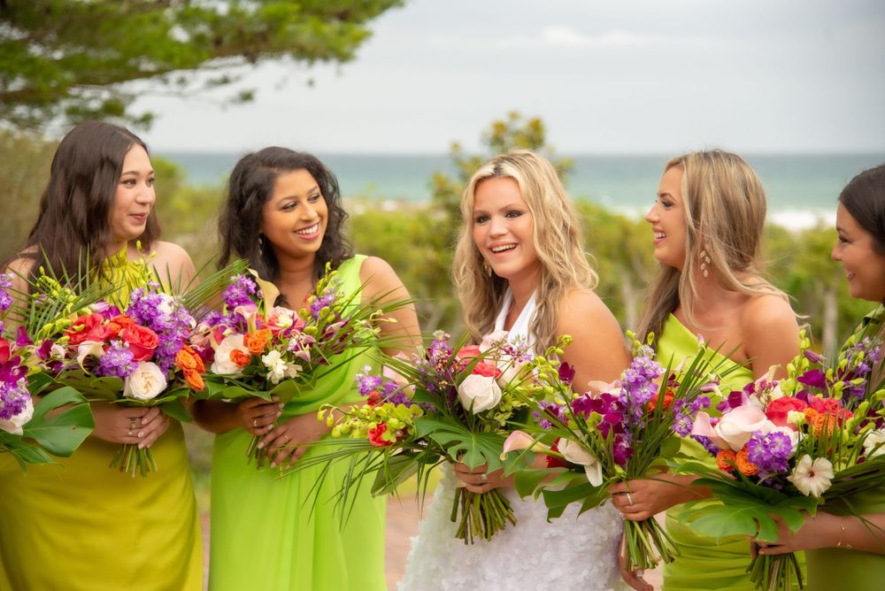 Bridesmaids in yellow dresses hold vibrant floral bouquets outdoors.