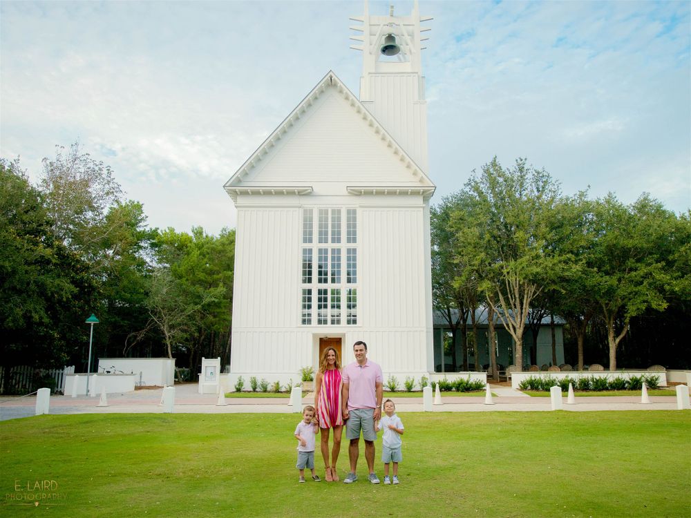 A family stands together on the lawn in front of a white chapel building.