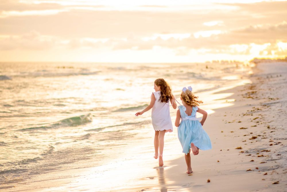 Two children run joyfully along the beach at sunset with golden light reflecting off the water.