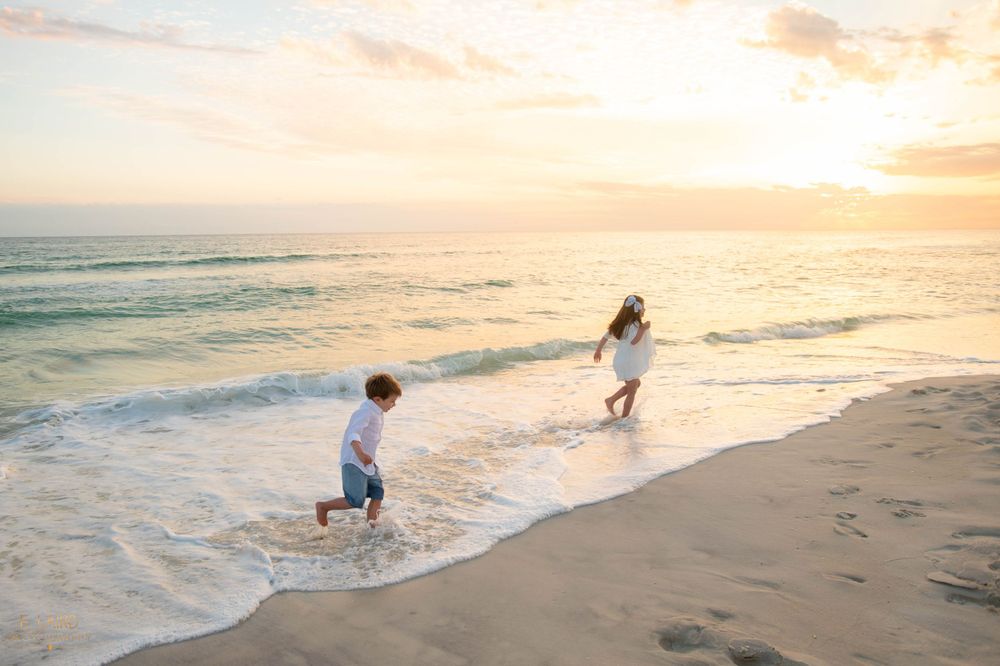 Two children play in ocean waves at sunset on sandy beach.
