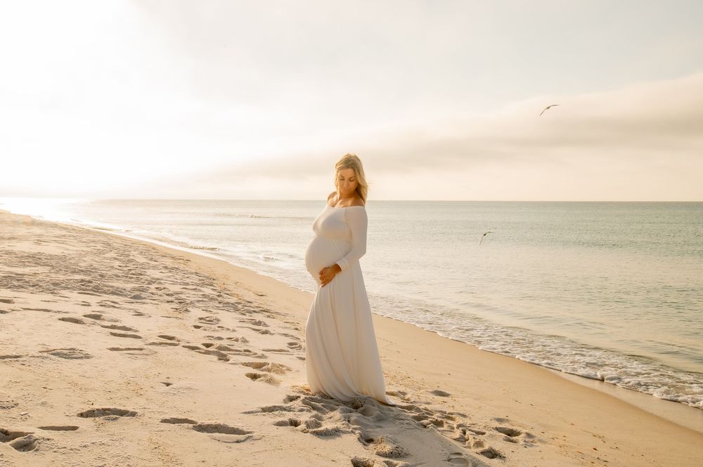 Woman in flowing white dress stands on beach during golden hour.