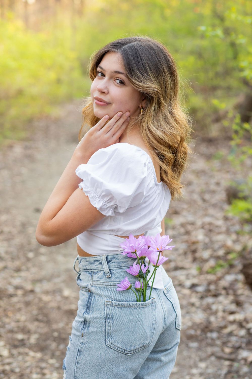 Creative portrait with purple flowers tucked into back jean pocket against natural outdoor setting.