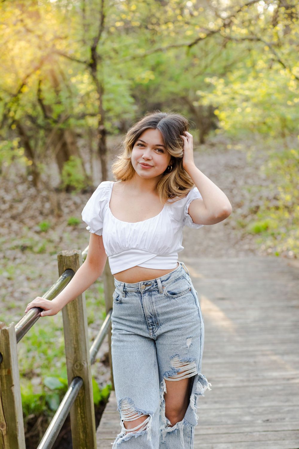 A casual outdoor portrait on a wooden walkway featuring ripped jeans and a white crop top.