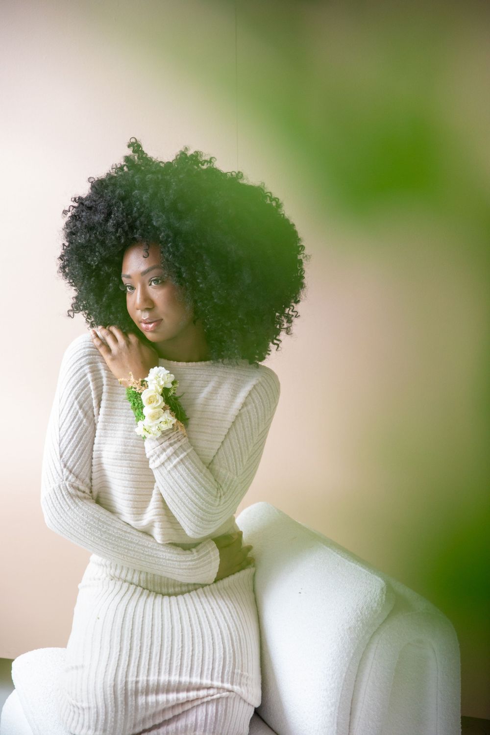 A woman in a white knit sweater dress poses elegantly against a soft green background with natural lighting.