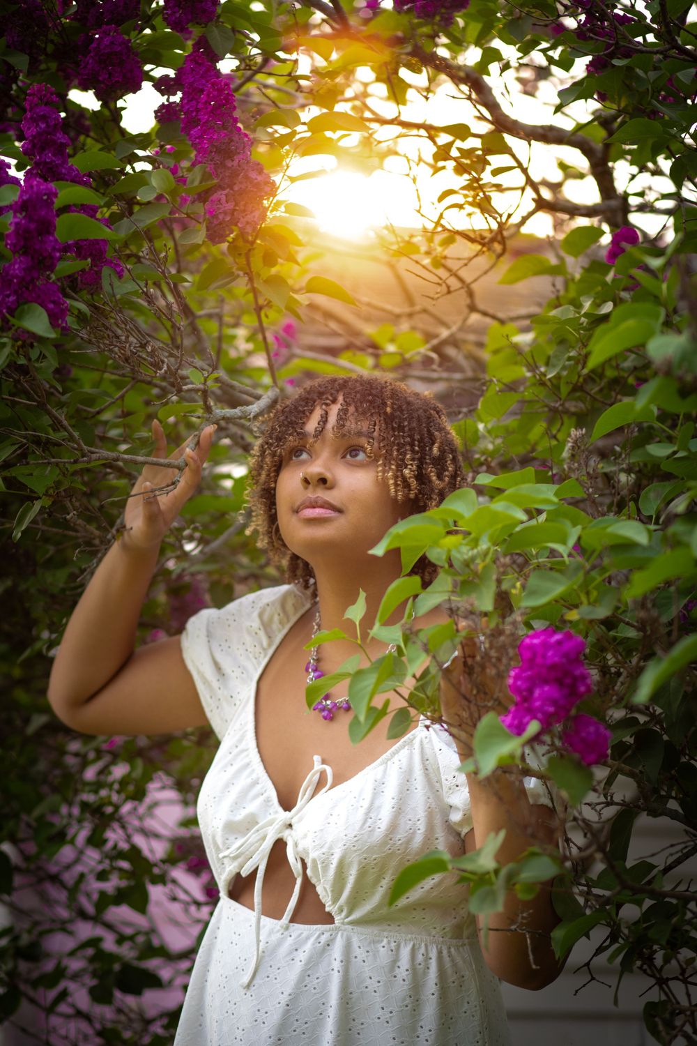 Artistic portrait in white dress among purple flowers with golden sunset light.
