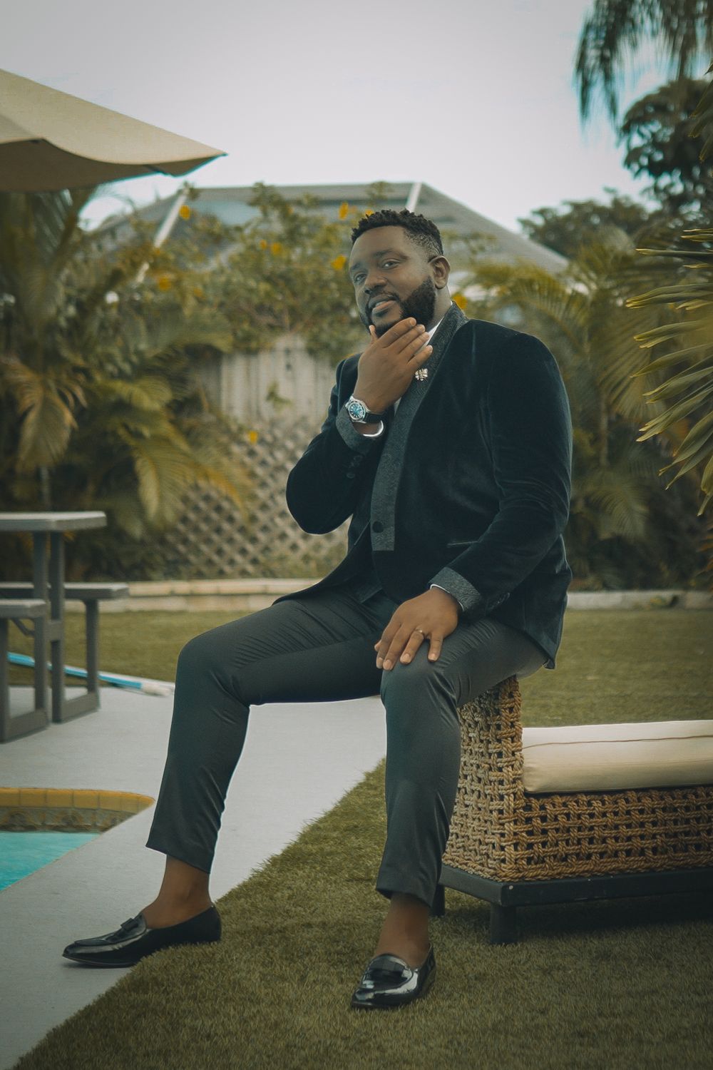Outdoor portrait in formal wear seated by pool with tropical landscaping.