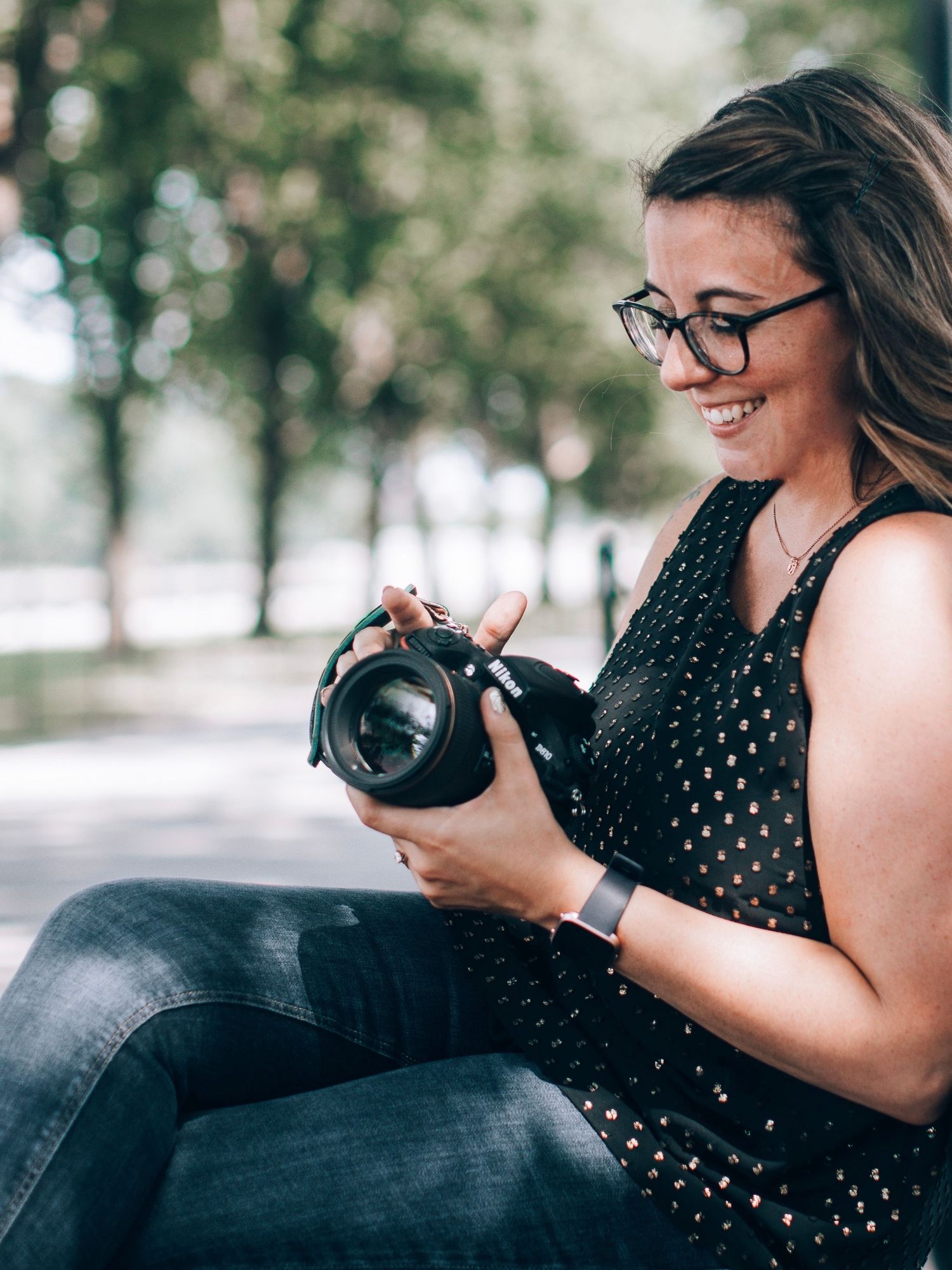 Photographer in polka dot dress smiling while looking at camera display outdoors.
