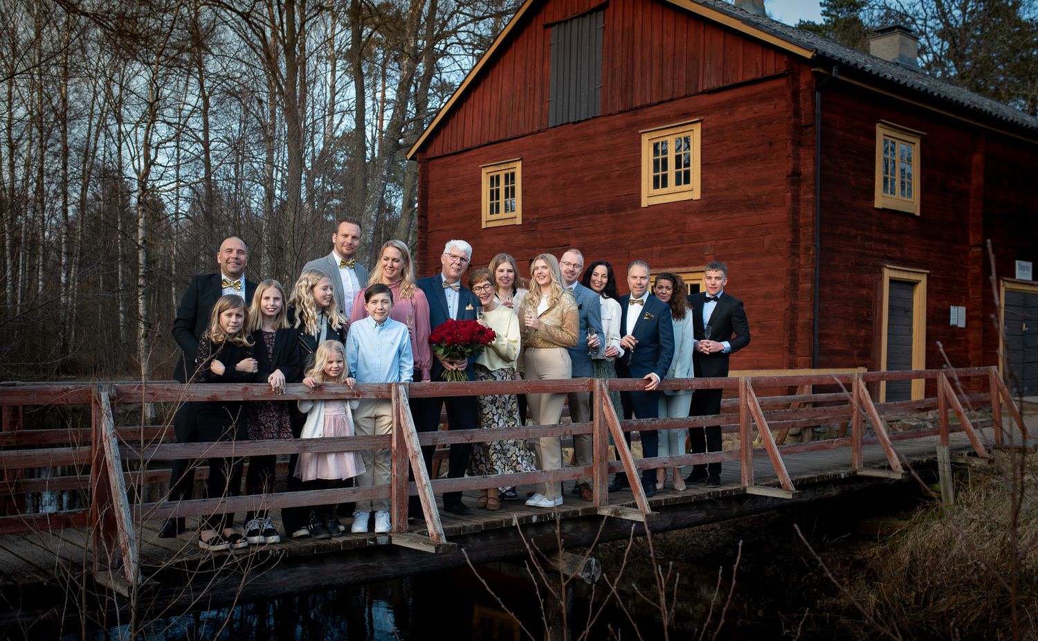 Wedding group photo on rustic bridge with red barn in background.