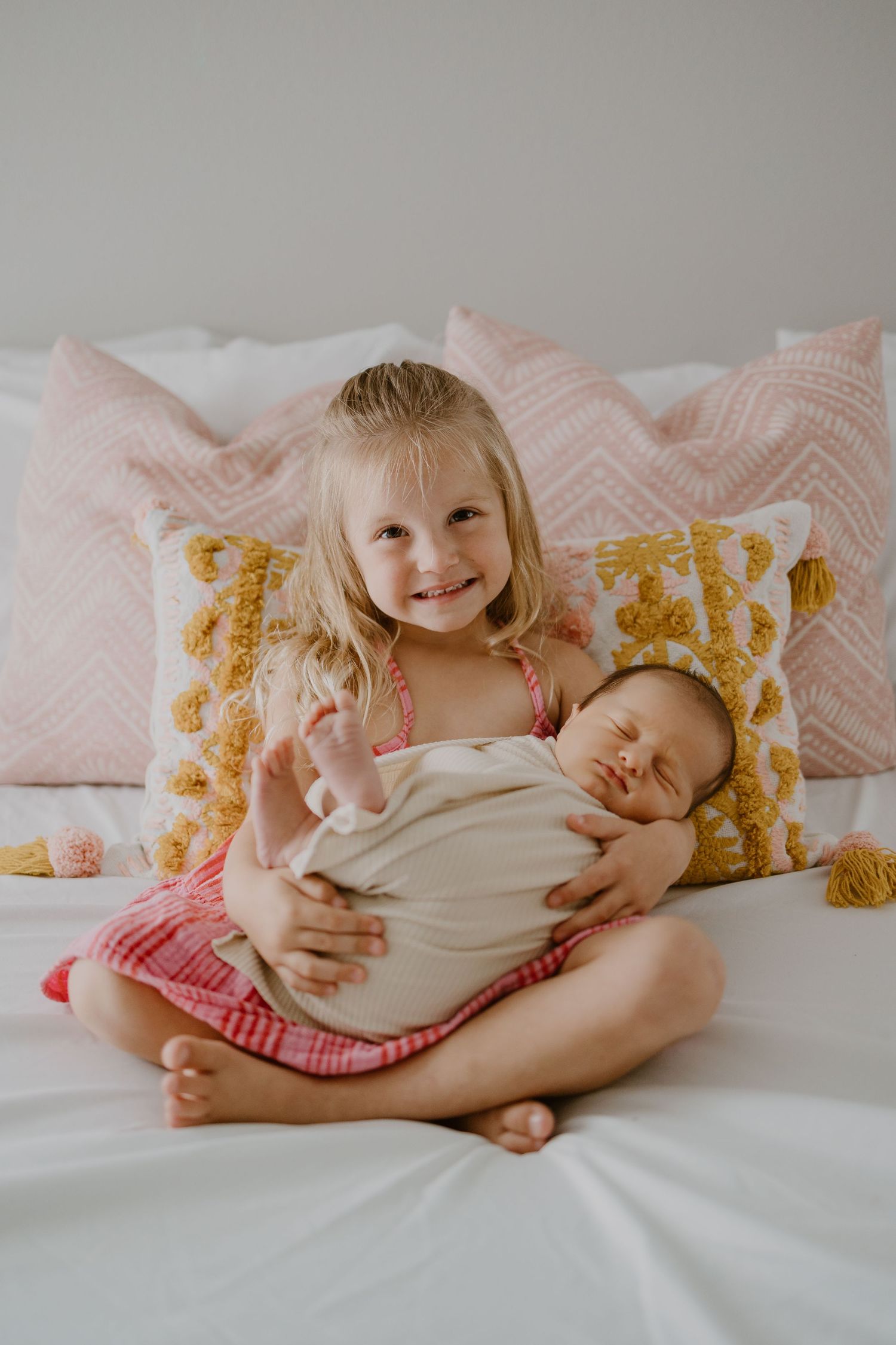 Two siblings sharing a tender moment while cuddling on a bed with floral pillows.
