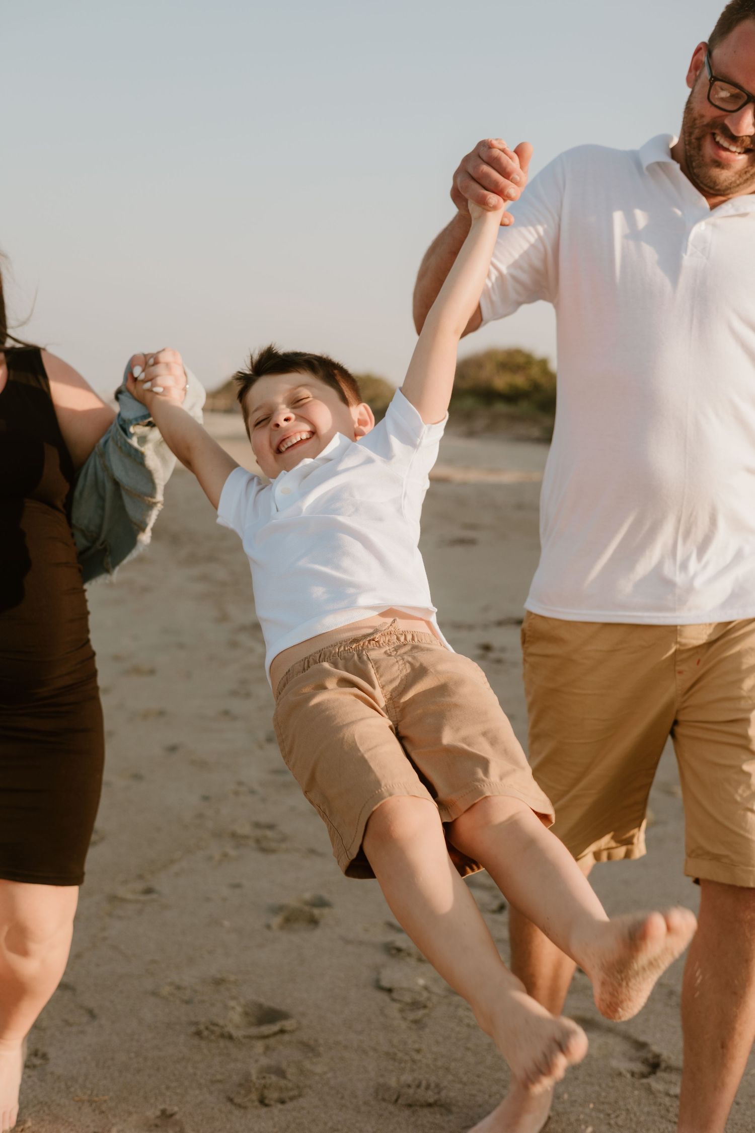 People in white shirts and khaki shorts jumping playfully on a beach.