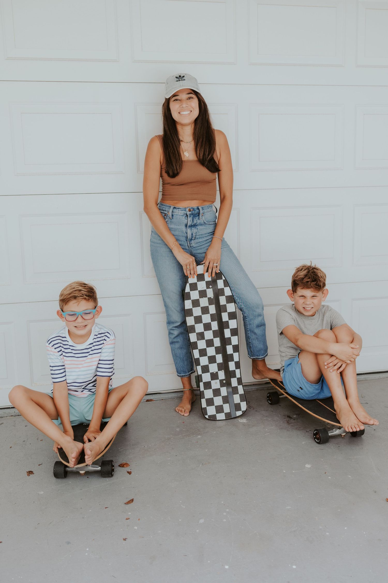 Group sitting against white garage door with skateboards and checkered bag.