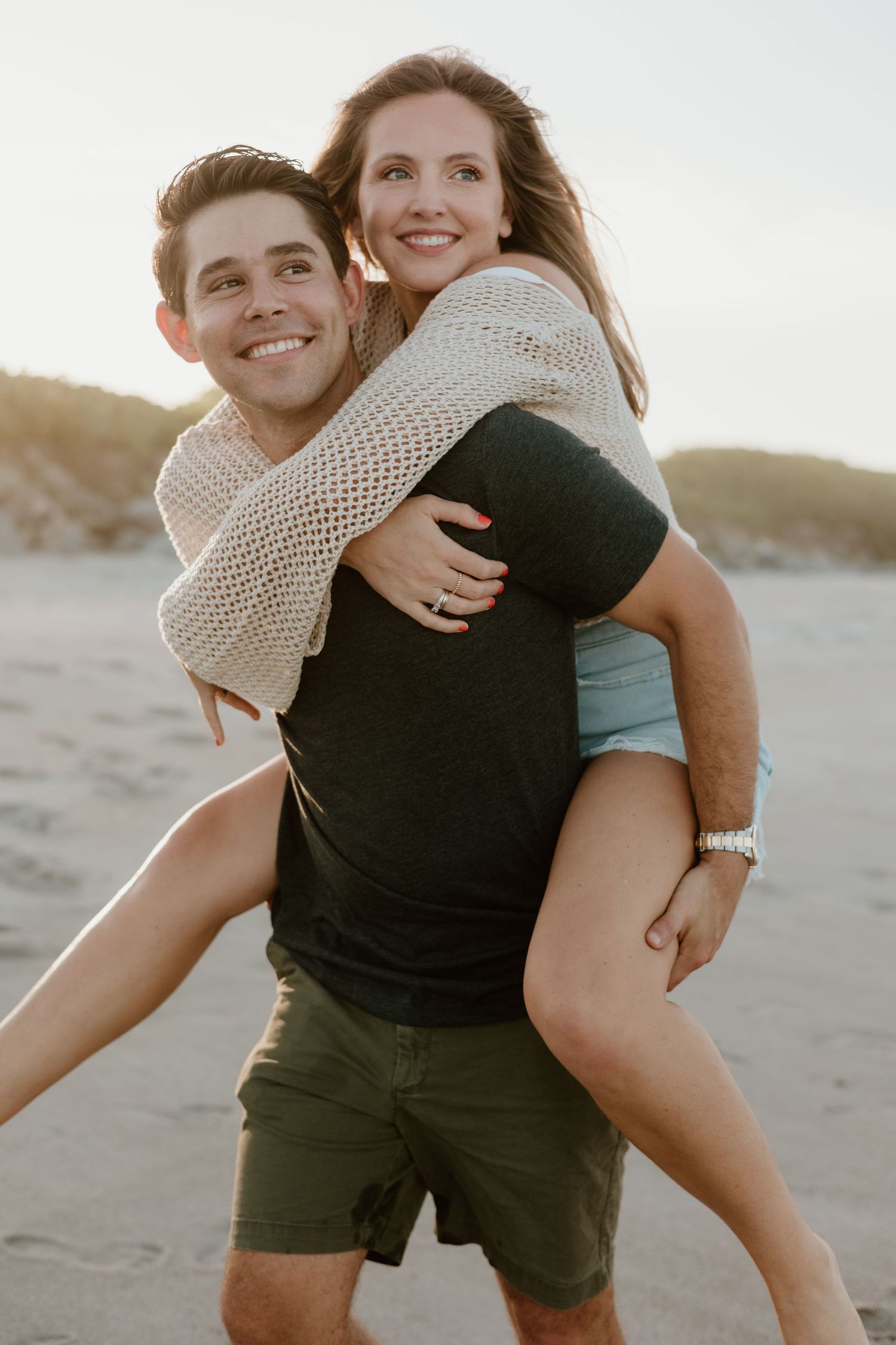 Playful piggyback ride moment on a sandy beach at sunset.