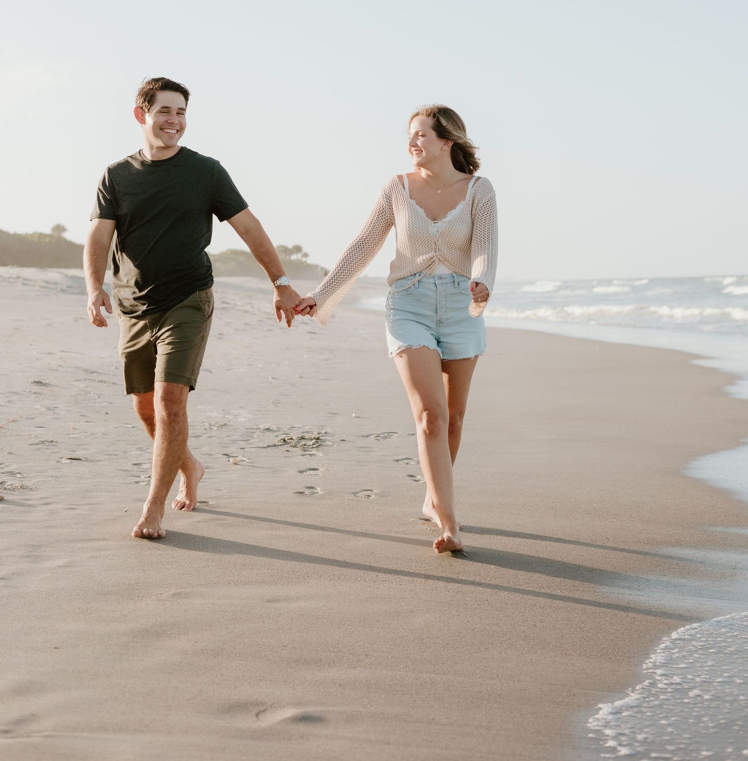 Couple running playfully along the beach shoreline at sunset.