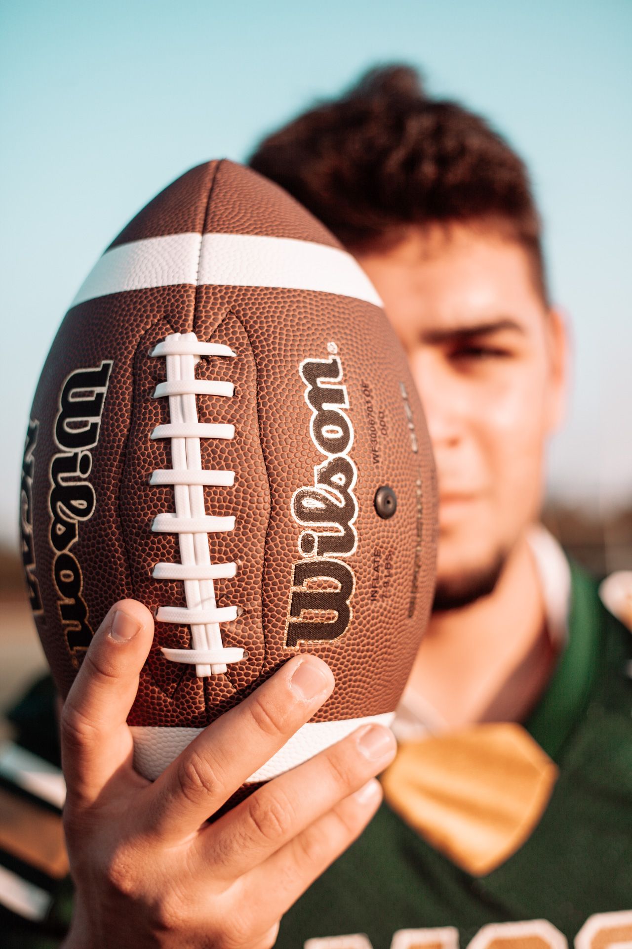 Close-up shots of hands holding football against blue sky background.