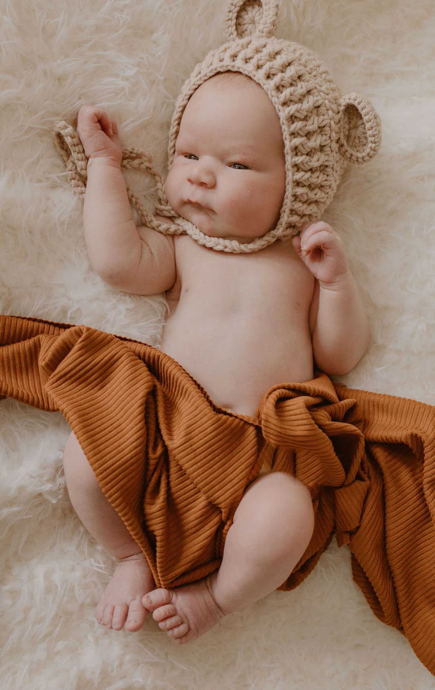 Baby wearing knit bonnet lying on orange blanket in sweet sleeping pose.