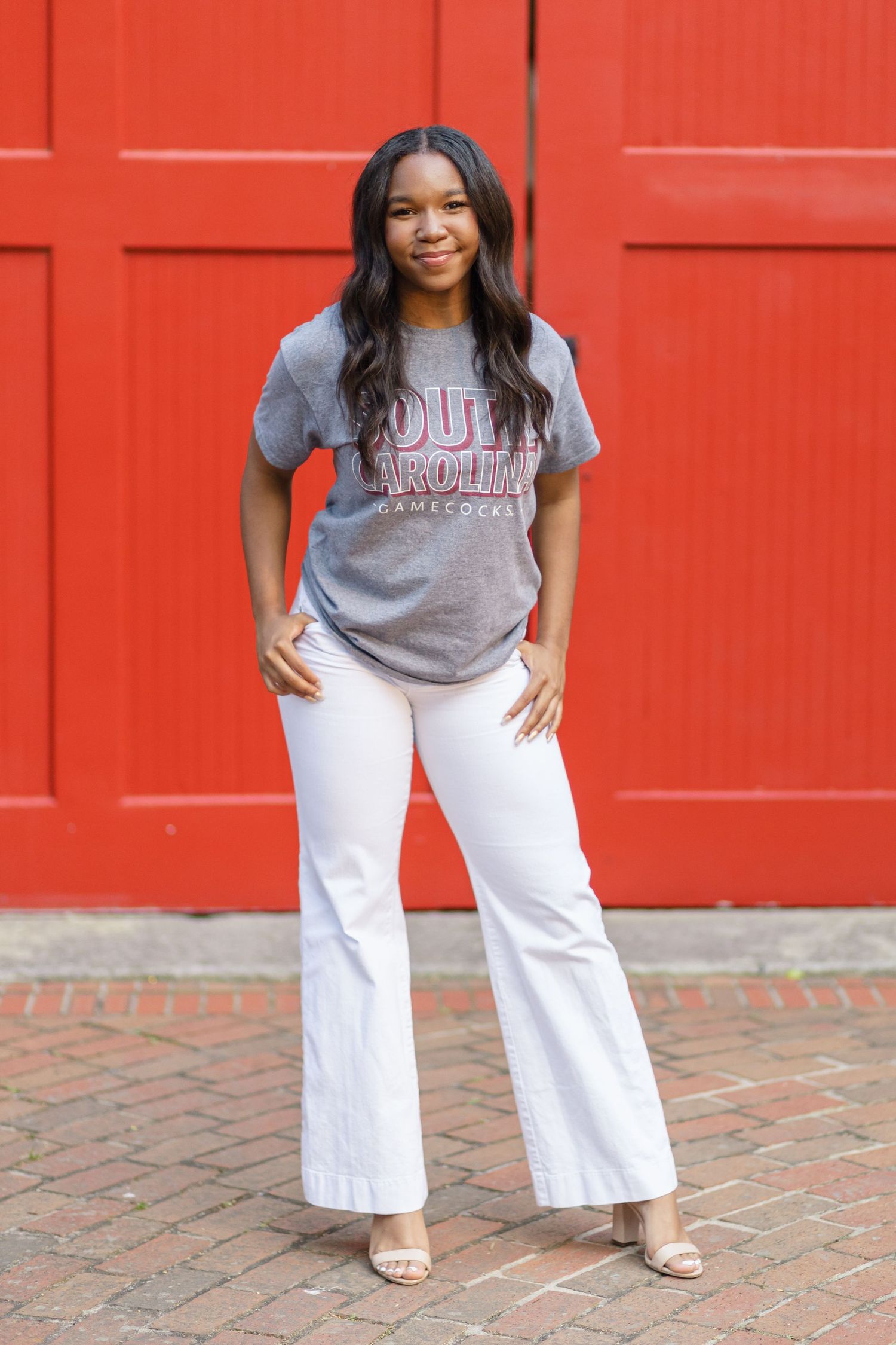 Casual portrait against bright red door wearing university t-shirt and white pants.