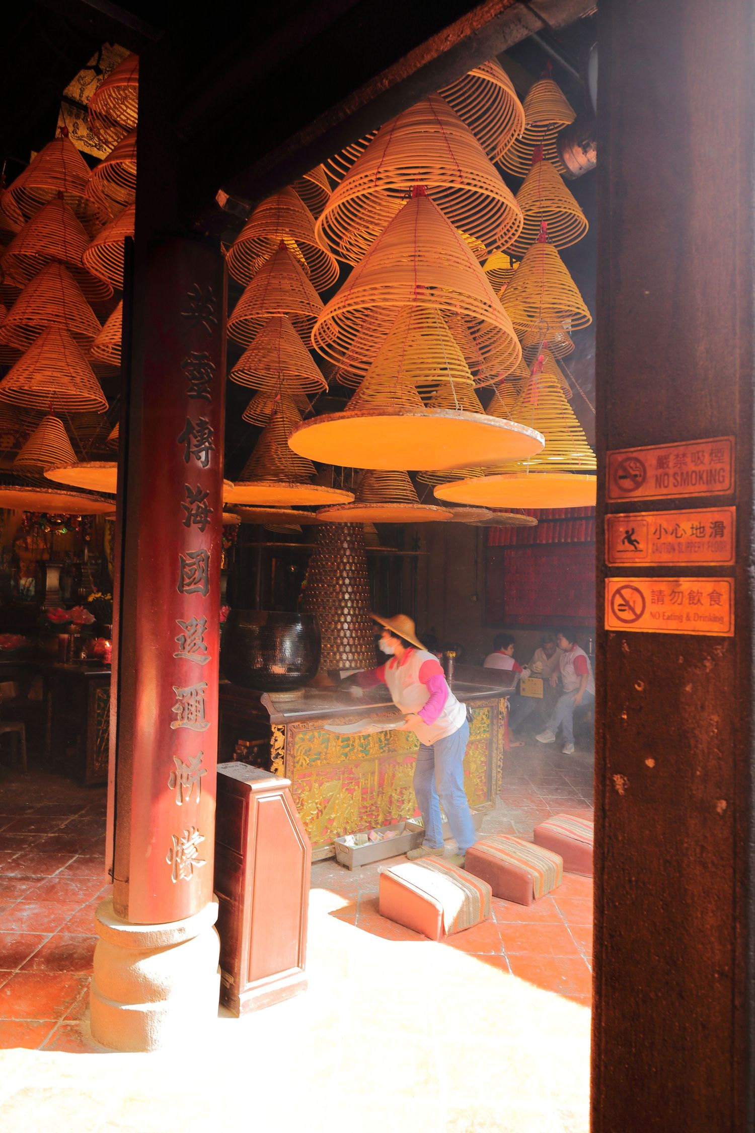 Temple interior with hanging spiral incense coils and red pillars.