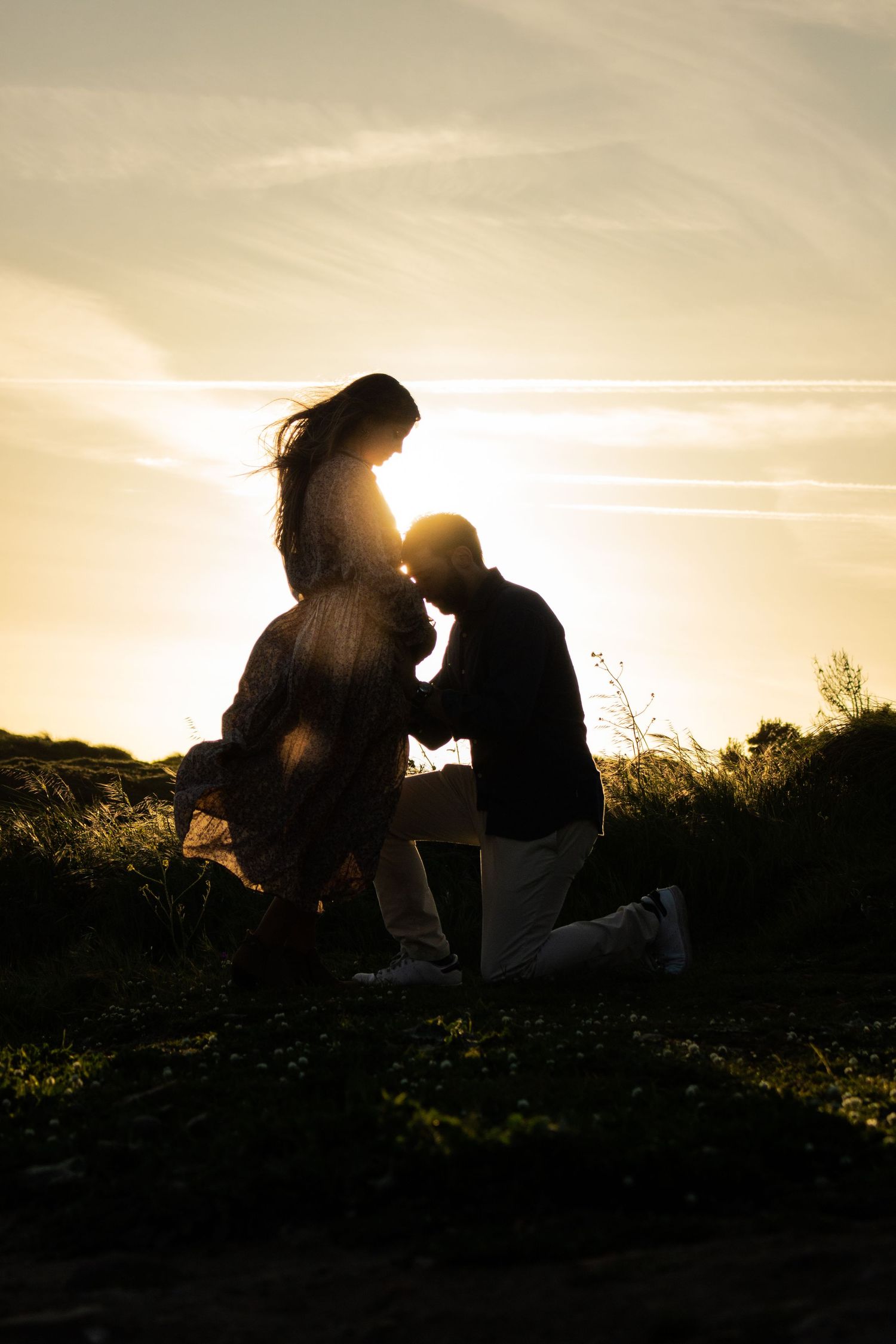 Silhouette of a romantic proposal at sunset in a field.