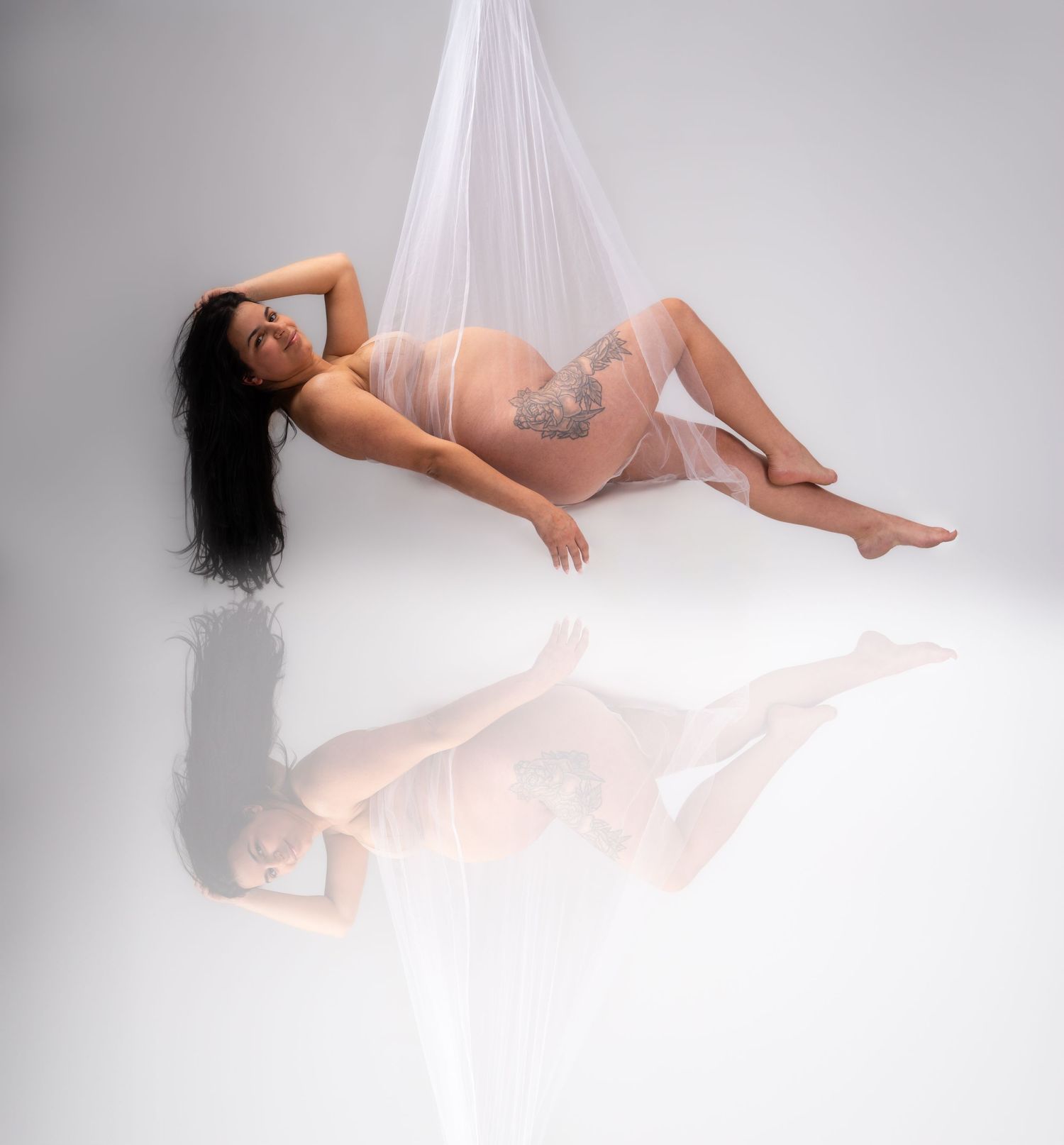 Artistic maternity photo with white fabric draping in studio setting.
