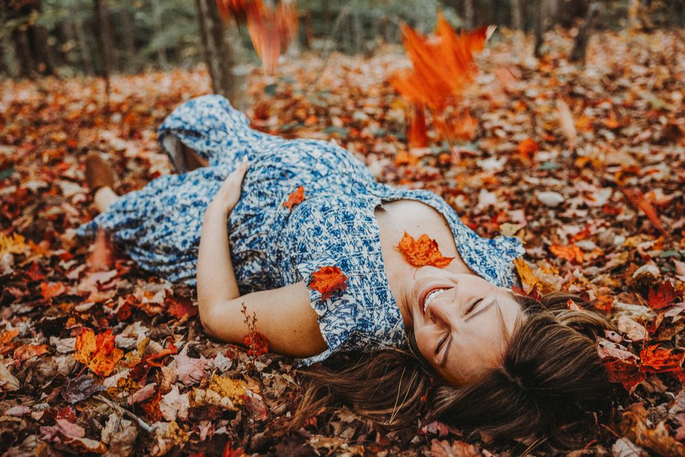 Pregnant woman wearing a blue dress and lying on the ground in the leaves.