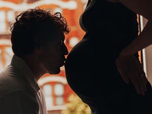 Silhouette of a pregnant woman's belly with her husband kissing her stomach.