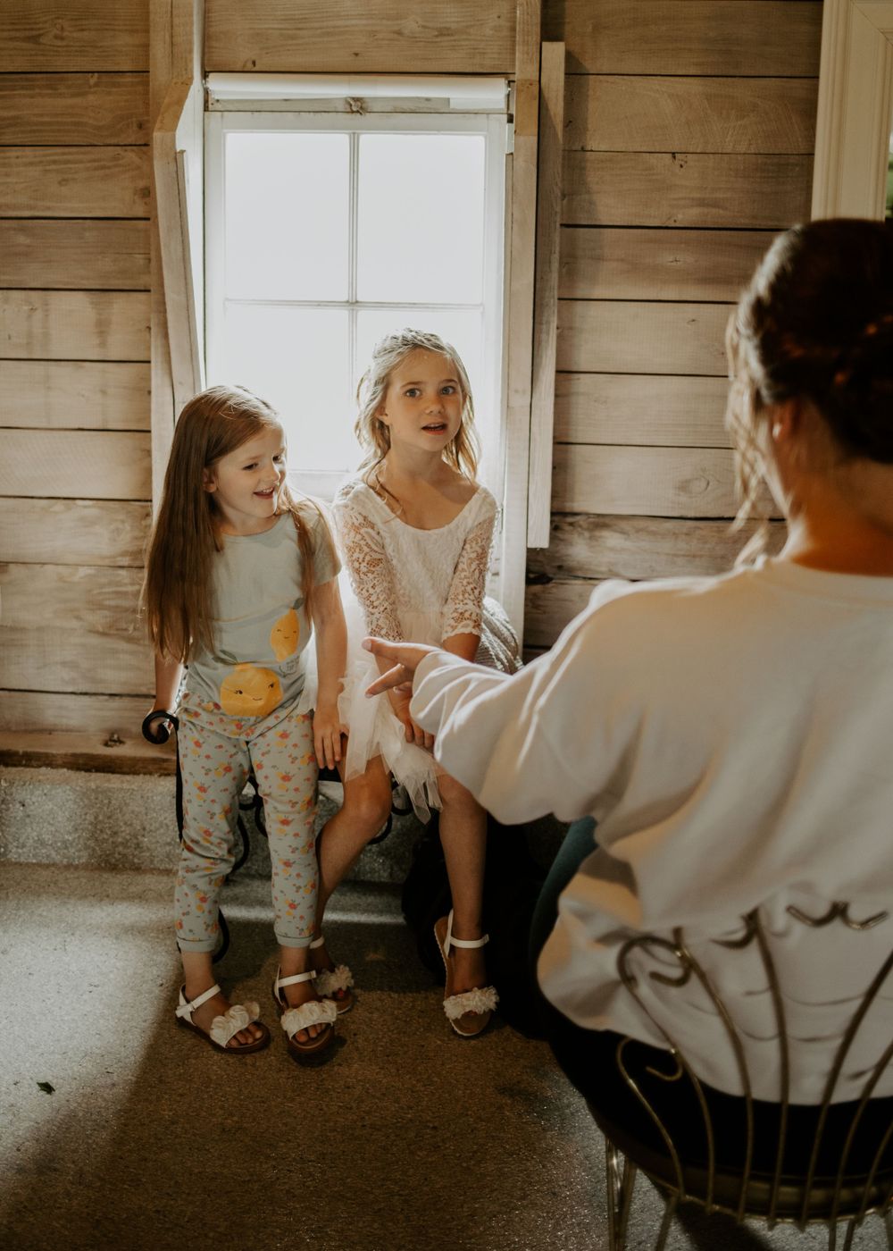 Two children sitting by window during wedding preparations in rustic wooden interior.
