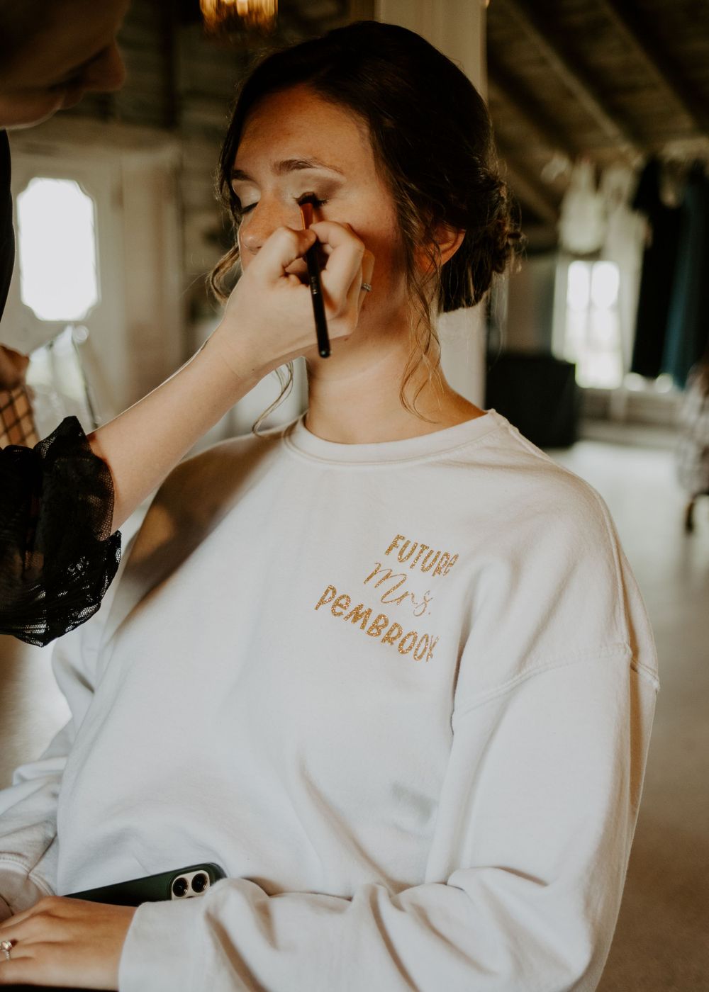Wedding preparation scene showing makeup application in white sweatshirt.