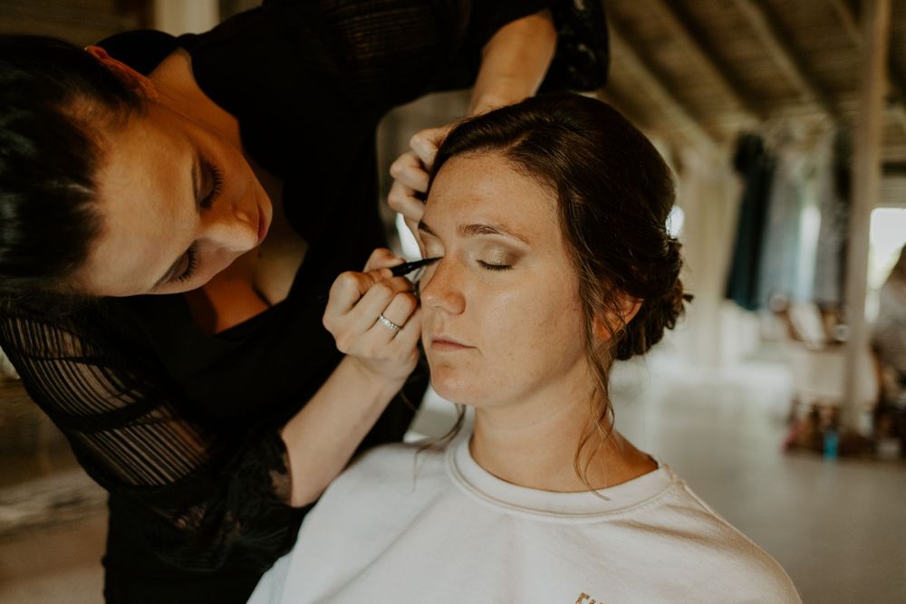 Professional makeup application during wedding preparations in rustic setting.
