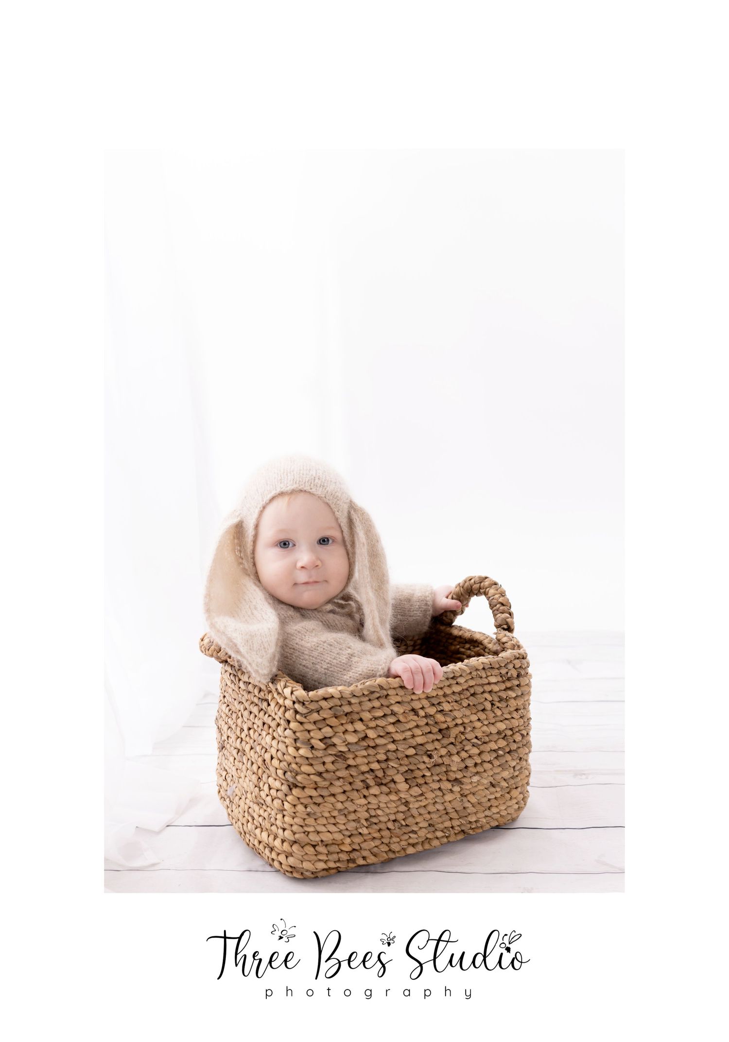 Baby wearing cozy outfit sitting in woven basket against white background in minimalist portrait.
