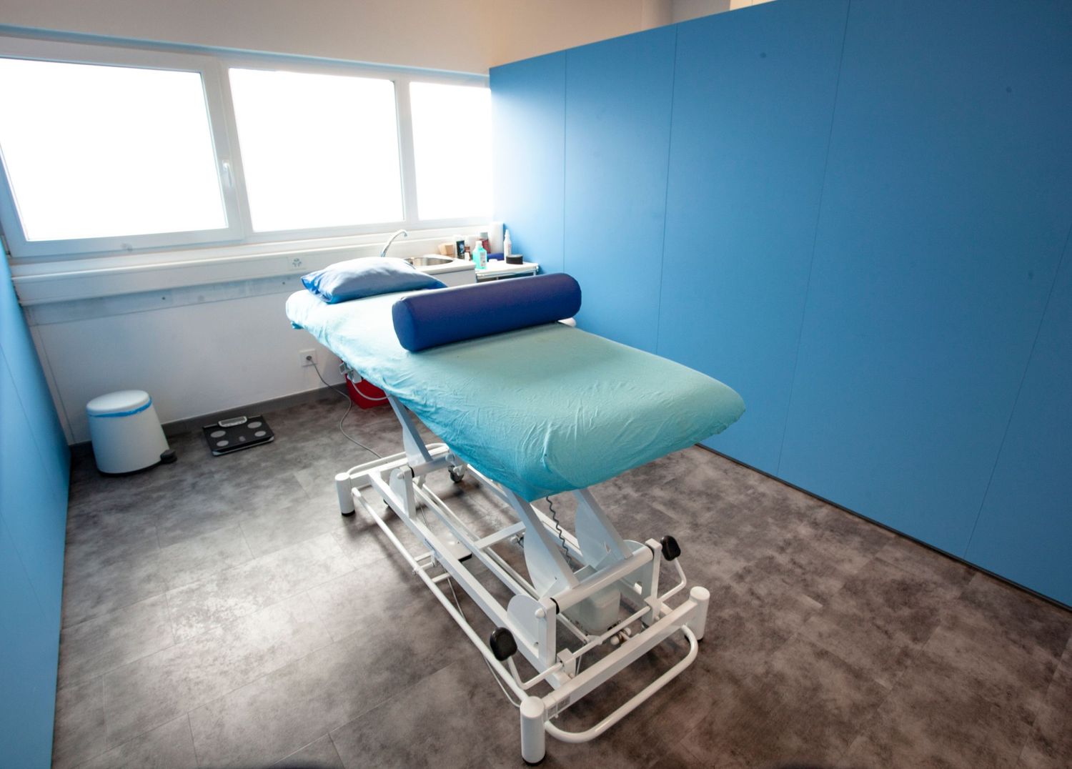 Medical examination room with blue walls and adjustable treatment table.