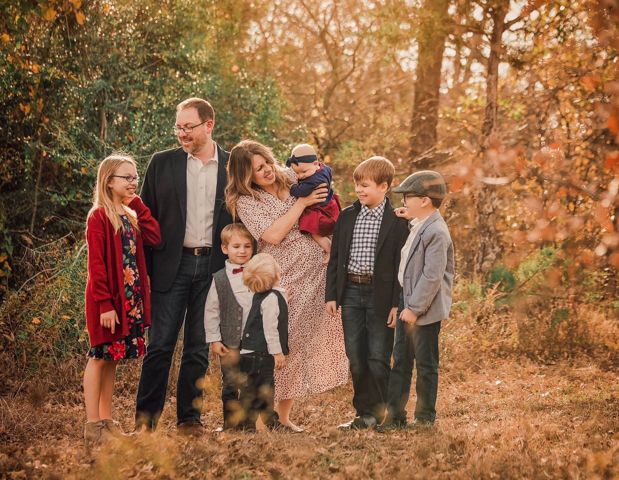 A family group portrait in autumn colors with fall foliage in the background.