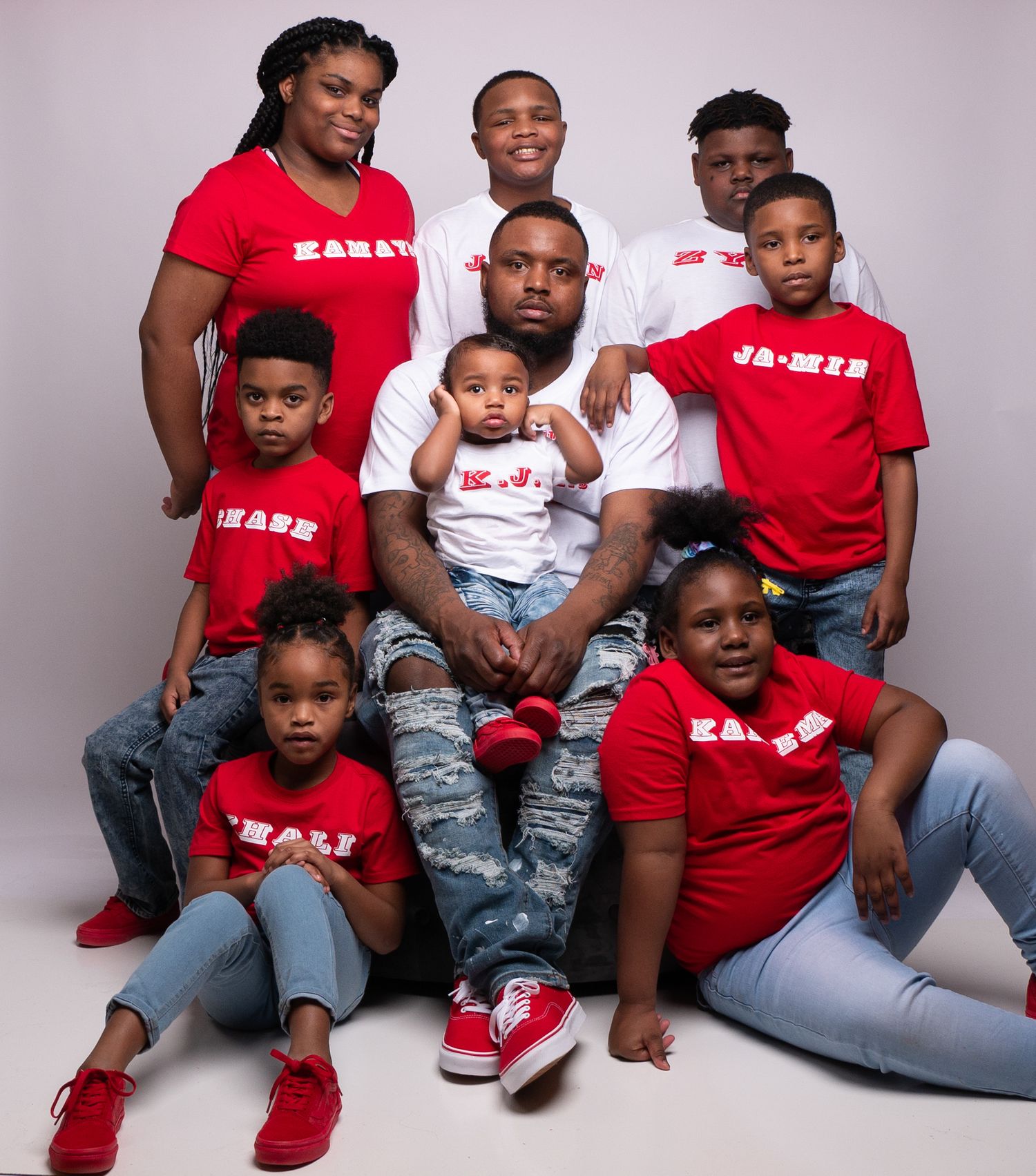 Professional studio photo of group wearing matching shirts in red and white against pink background.