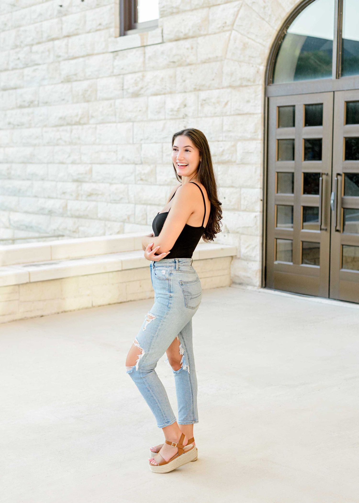 Candid lifestyle portrait in casual summer attire against white stone building with architectural details.