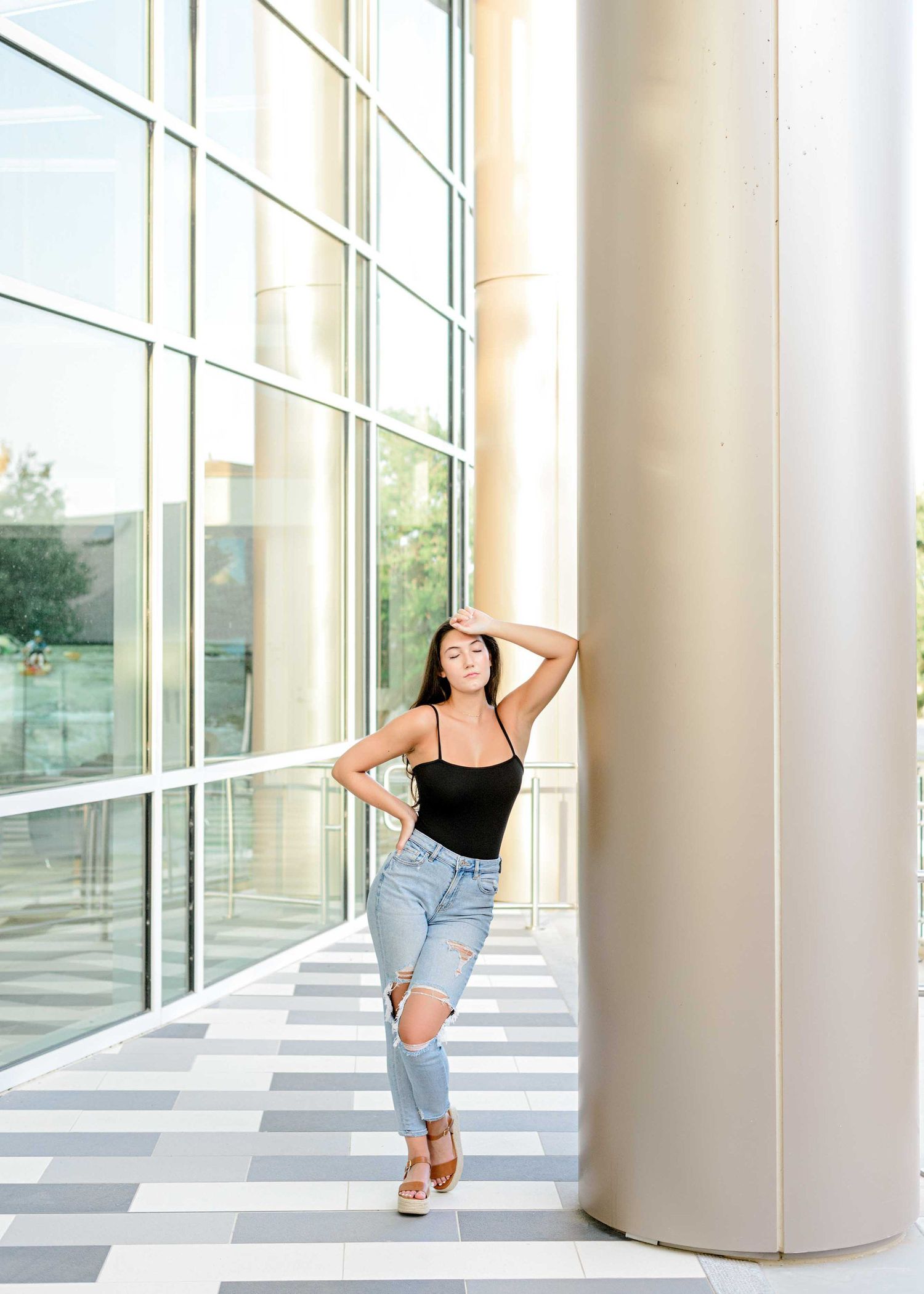 Stylish casual pose against modern architecture with striped floor pattern and glass windows.