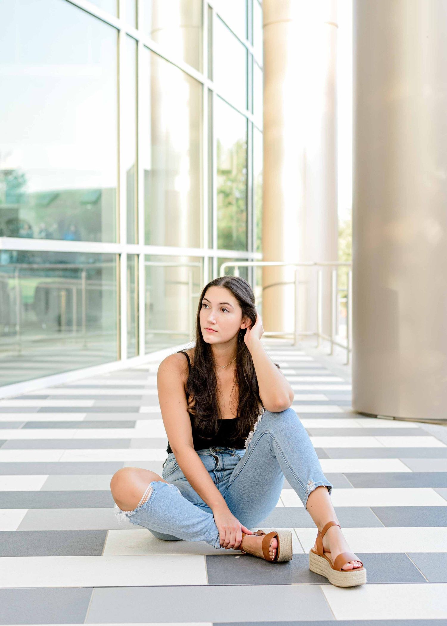 Relaxed seated portrait on geometric flooring with glass wall backdrop.