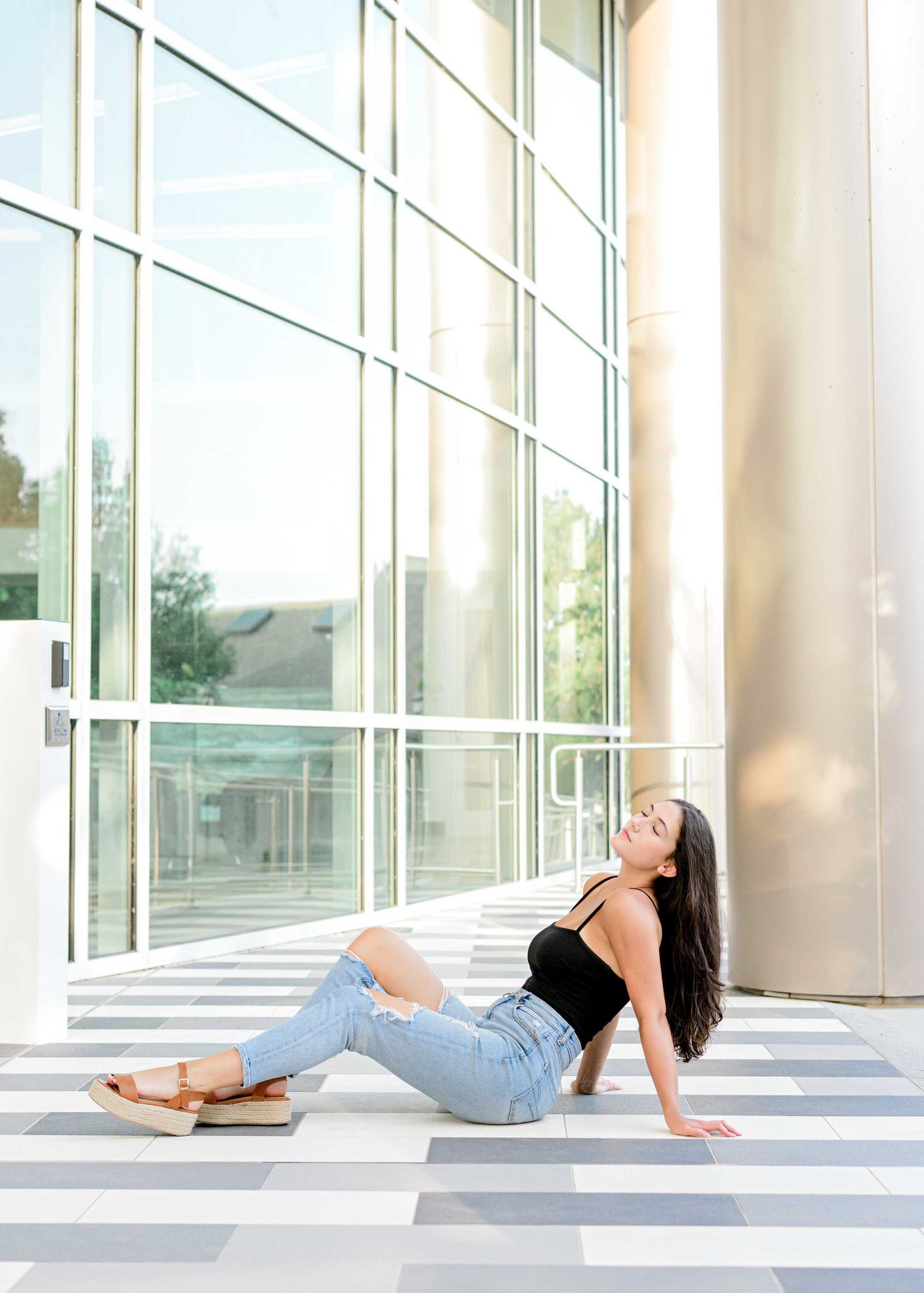 Casual lifestyle pose on striped floor against glass windows and concrete columns.