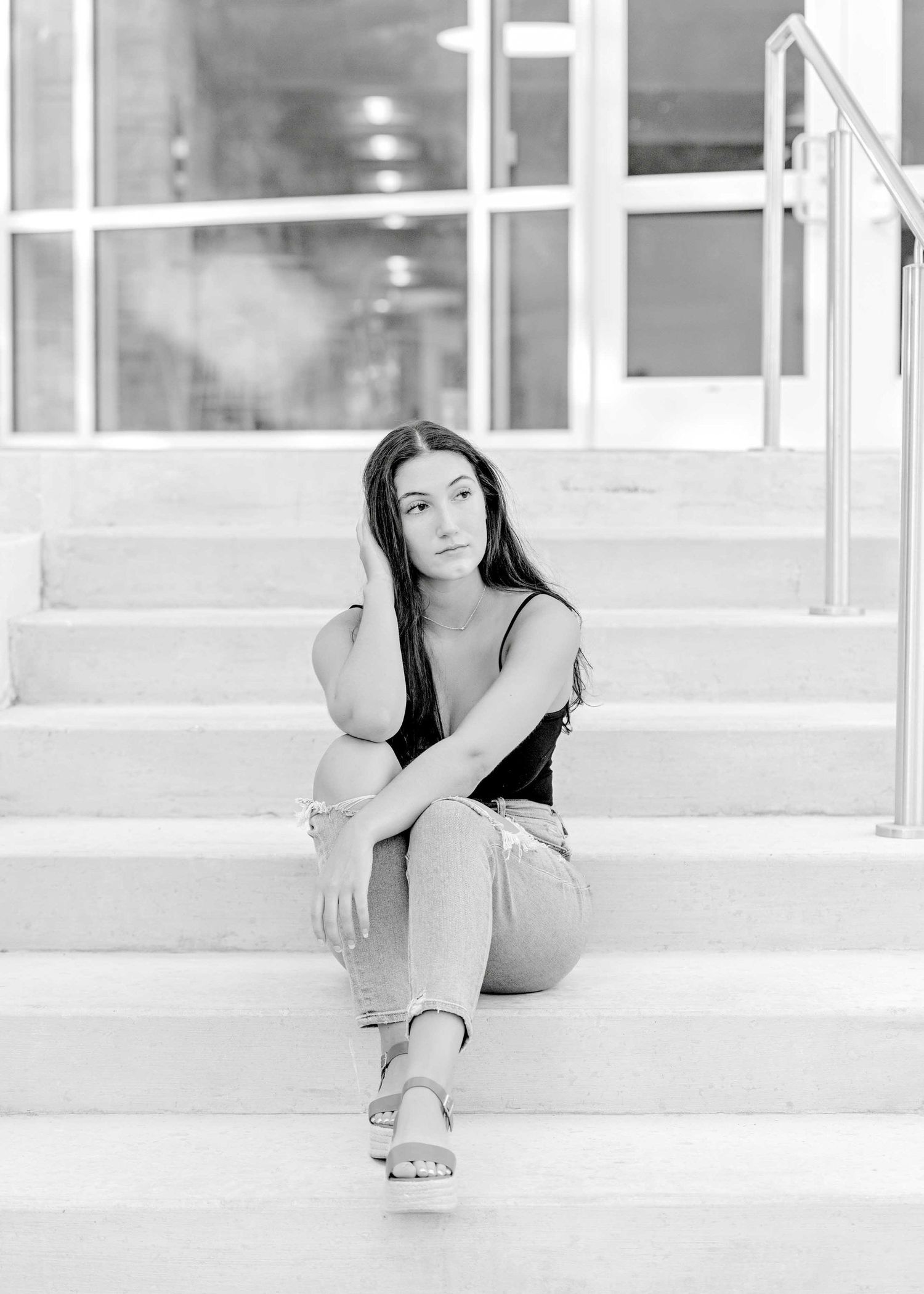 Black and white portrait of a casual outfit with light jeans and tank top on concrete steps.