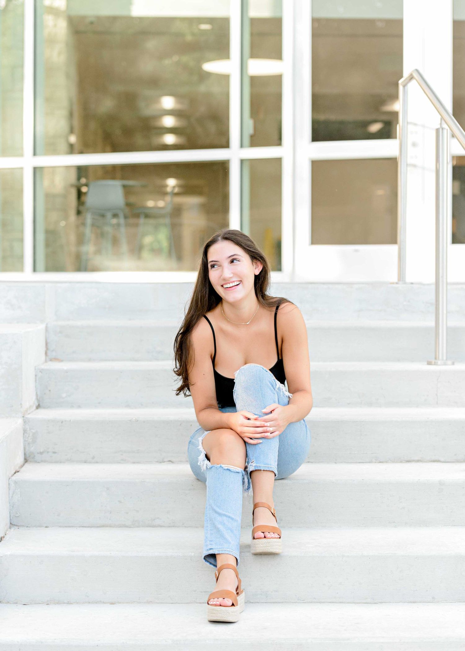 Lifestyle portrait on white concrete steps wearing light denim and sandals in natural lighting.