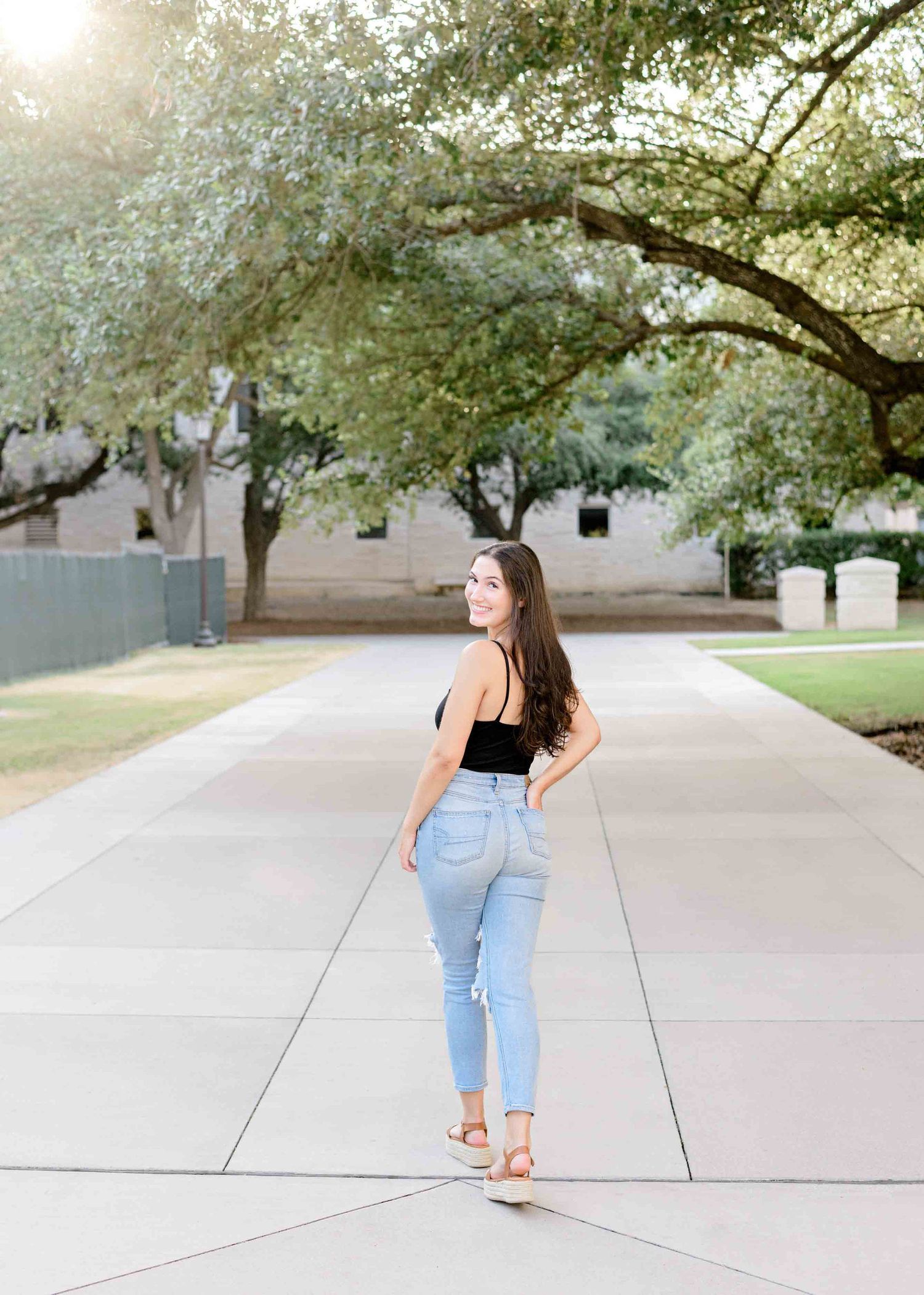 Lifestyle fashion photo showing casual summer outfit on walkway with blooming trees.