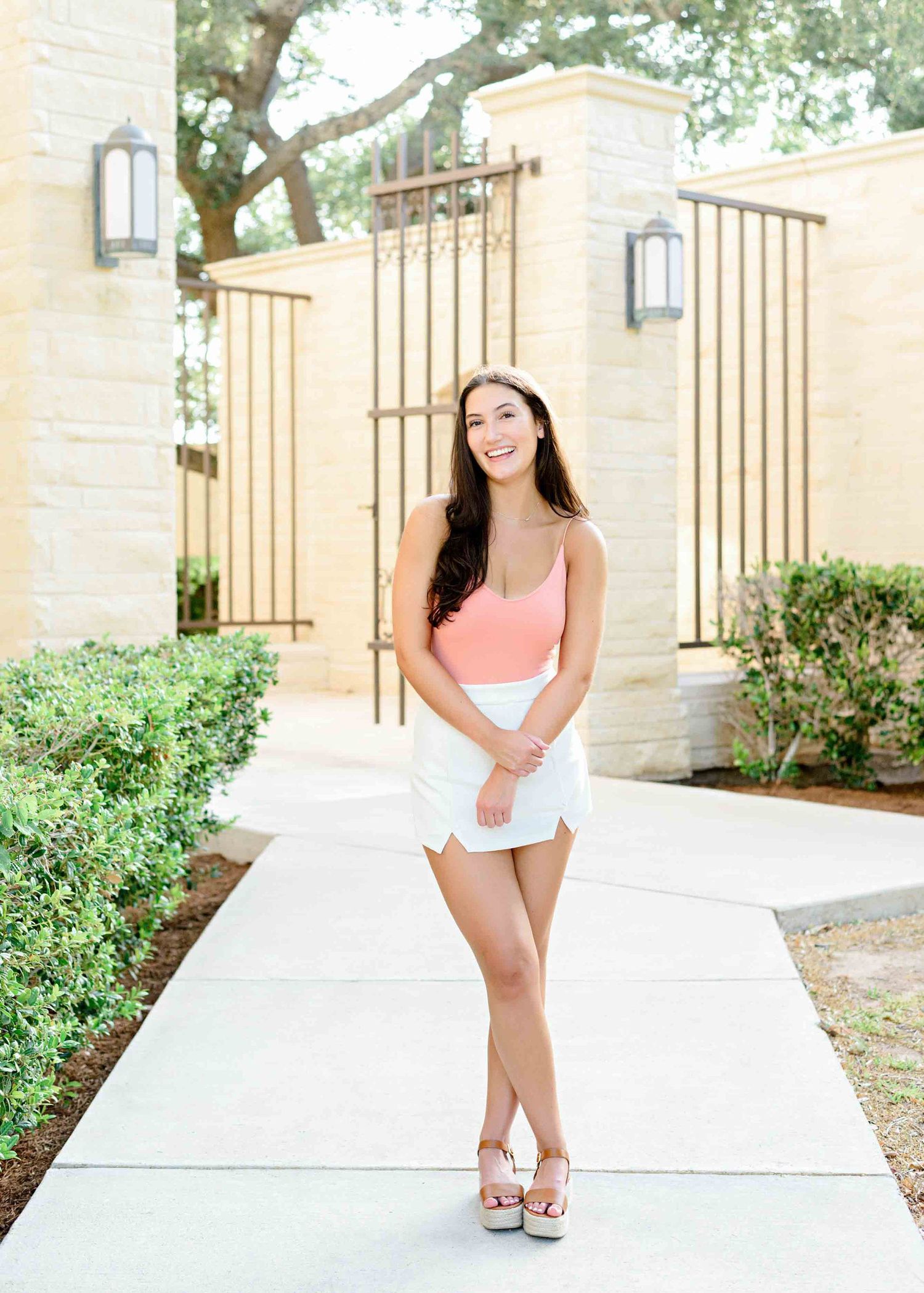 Summer fashion portrait in front of ornate gates wearing coral tank top and white skirt.