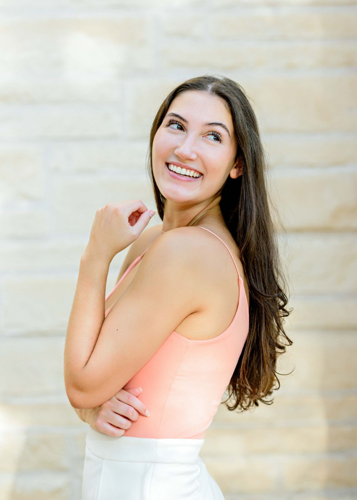 Portrait against stone wall wearing coral sleeveless top with natural lighting.