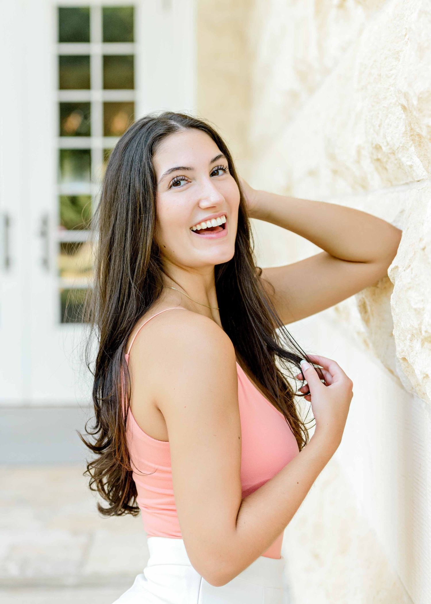 Summer portrait session against light stone wall wearing coral tank top.